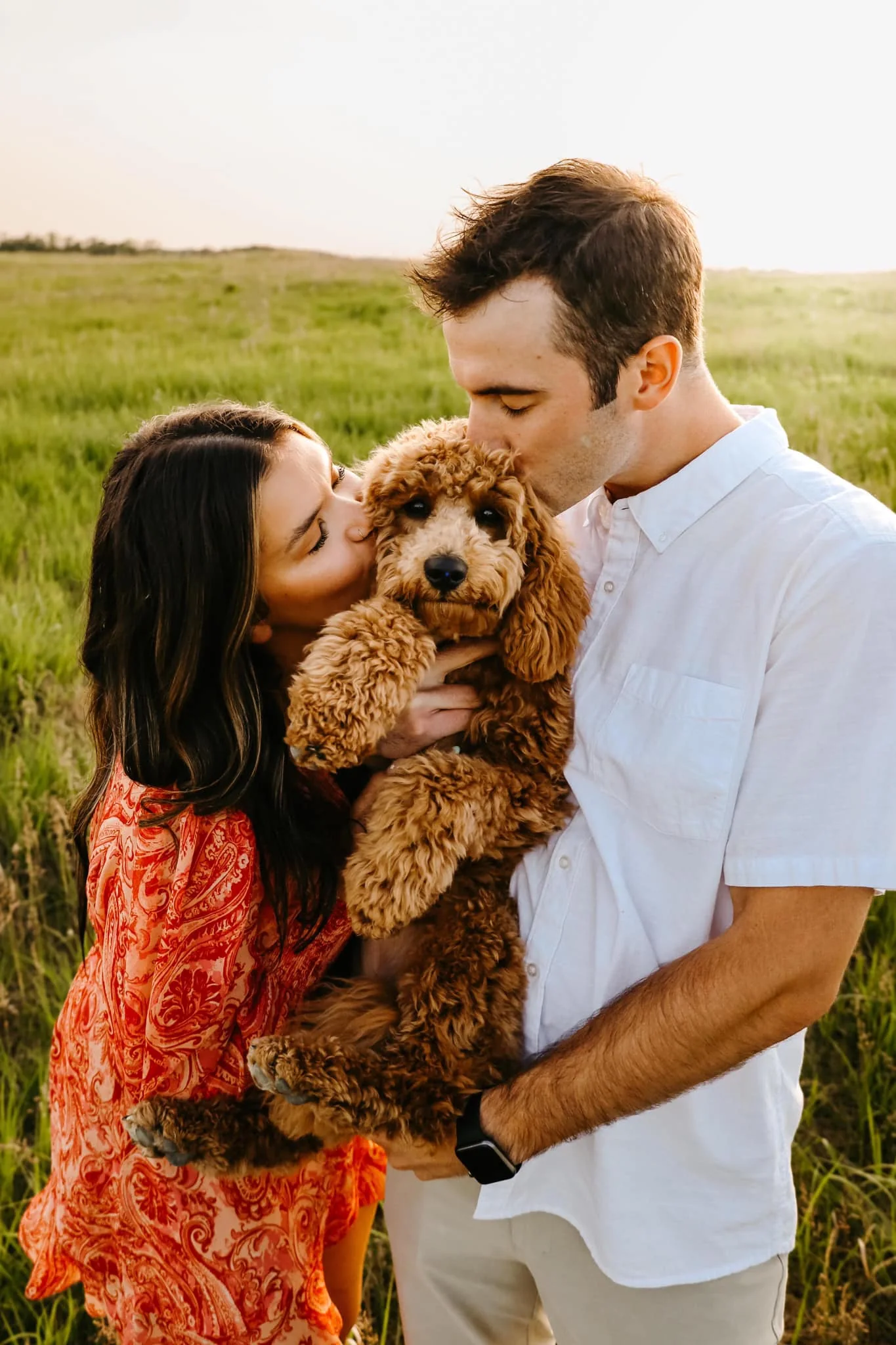 A couple holding and kissing their Goldendoodle puppy